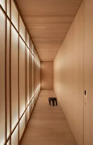 A minimalist corridor with wooden walls and floor. A small black stool is placed near the end.
