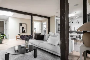 A minimalist living room with a grey couch, a black coffee table, and a vase with purple flowers on a rug, with a connected m