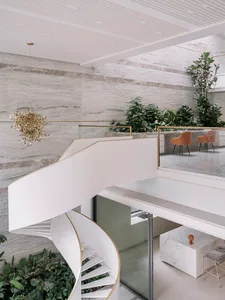 White minimalist staircase with marble floors, concrete walls, and a gold chandelier in a modern office setting.