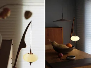 A modern kitchen interior featuring wooden furniture, glass pendant lights, and a bowl of fruits.