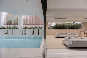 Modern minimalist living room with concrete walls, glass windows, and marble furniture.