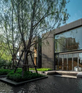 A modern residential exterior featuring a combination of wood and glass materials, set against a natural tree and water featu