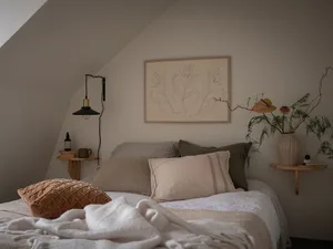 A neatly made bed with a minimalist design, featuring fabric bedding and a wooden frame, surrounded by natural light and simp