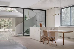 A minimalist kitchen featuring a marble island with two transparent chairs and a large window.