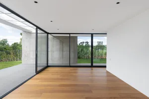 Modern minimalist living room with concrete walls, large glass windows, and wooden flooring.