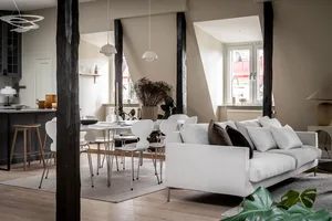 A modern living room with a white sofa, wooden flooring, and a table with chairs.