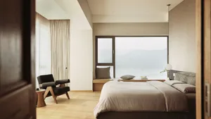 A modern minimalist bedroom with a large window overlooking mountains and a serene view.