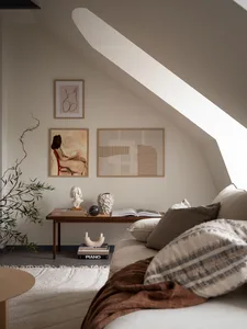 A minimalist living room with a beige couch, a wooden coffee table, and several wall-mounted artworks.