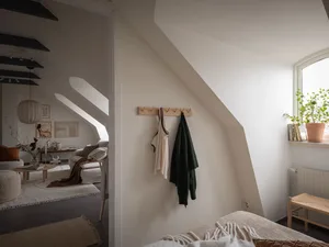 A minimalist bedroom featuring neutral tones and textiled fabrics hanging on a hook on the wall.