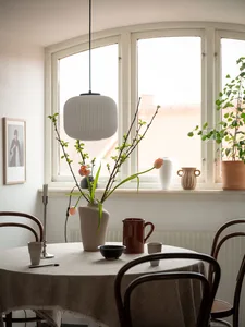 A cozy kitchen scene featuring a ceramic vase with branches and tulips, a mix of ceramic dishes, and soft lighting from a pen