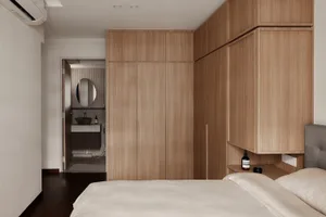 A minimalist bedroom featuring wooden cabinets, a white quilt, and a view into the attached bathroom with a circular mirror a