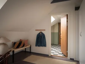 A minimalist entrance area with a wooden door, checkered floor, and a bench with pillows.