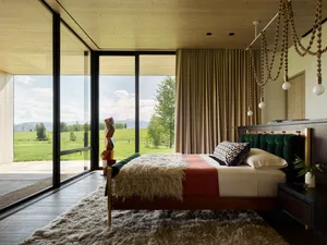 A modern bedroom featuring a bed with green and red bedding, a wooden headboard, and a large window overlooking green fields 