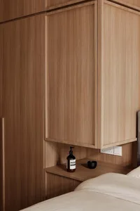 A modern bedroom featuring a wooden cupboard with built-in shelves and a black bottle of lotion.