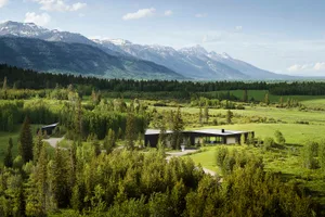 Modern house nestled in a forested valley with a lake nearby.