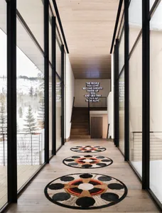 Modern interior design hallway with wooden floors, glass walls, and circular textiles on the floor.