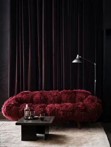 A modern living room featuring a plush, burgundy velvet couch, a black coffee table with a whiskey bottle and glasses, and a 