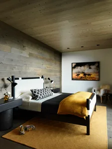 A minimalist bedroom with a wooden bed, white and yellow linens, and a textured rug.