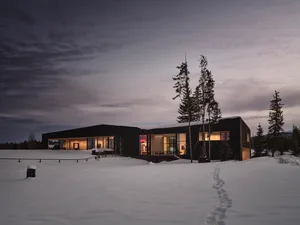 A modern house with wooden exterior and metal accents nestled in a snowy landscape with a twilight sky.