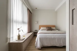 A minimalist bedroom with a wooden bed and wooden storage bench alongside the window, featuring sheer and light-colored curta
