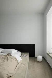 A minimalist bedroom with a concrete floor, wood headboard, and clean, simple design.