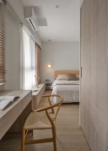 Minimalist bedroom with a wooden bed frame, white bedding, and a woven chair.