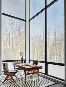 A minimalist home office with a wooden desk and chair, featuring large windows with a snowy forest view.