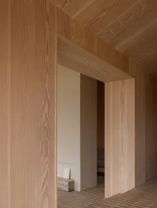 Detail of a minimalist interior with wood paneling against a clean white wall and wooden flooring.