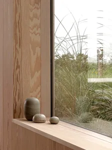 Wooden sculptures on a wooden window sill with tall grasses outside the window.