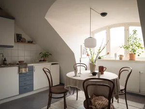 A minimalist kitchen with wooden furniture, a round table, and a window with greenery.