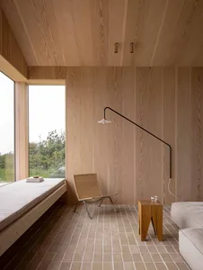 A minimalist living room featuring wood-paneled walls and a window seat with a wicker chair.