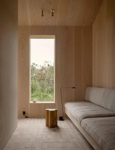 A minimalist living space featuring a concrete floor, wooden walls, and a small sofa with a floor lamp.