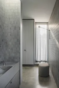 A modern bathroom featuring concrete-tiled walls and flooring, with a concrete sink and minimalist design elements.