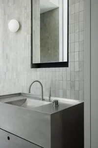 A modern minimalist bathroom with metallic sink and square tiles.
