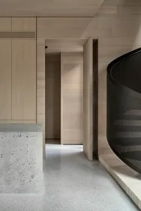 A modern interior space featuring wooden walls and floor, with a concrete bench and a curved metal railing.