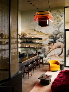 A modern living room bar featuring a yellow chair, red sofa, and a mountain mural backdrop.