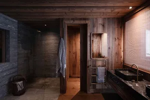 A modern, industrial-style bathroom with wooden walls, a stone sink, and a glass shower enclosure.