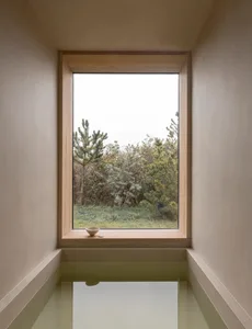 A minimalist bathroom with a glass window, wooden accents, and a concrete bathtub.
