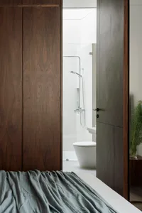 Modern minimalist bathroom with white tiles, glass shower enclosure, and sleek, dark wooden cabinetry.