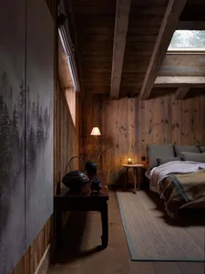 Minimalist bedroom with wooden furnishings, including a bed, table, and lamp.