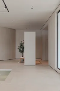 A minimalist interior space with a white column, grey walls, and a small green plant in a vase on a table.