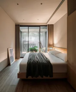 A modern bedroom with a wooden floor, a bed covered with a striped blanket, and a framed artwork leaning against the wall.