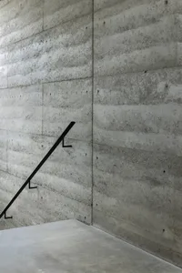Concrete staircase with black handrail against a textured concrete wall