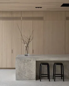 Modern minimalist kitchen with concrete countertop, black stools, and wooden cabinets.
