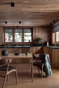 A modern minimalist kitchen with wooden elements, featuring a wooden dining table and chairs, black countertops, and a window