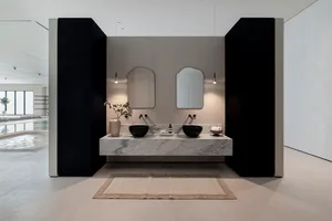Minimalist modern bathroom with marble countertops and sinks, featuring a vase with greenery and two arched mirrors.