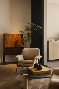 A modern living room featuring a beige textured armchair, a green marble coffee table, and a wooden cabinet with a plant。