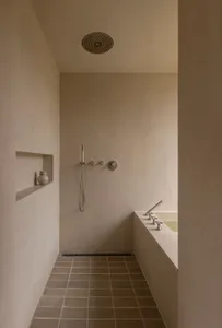 A modern minimalist shower stall with concrete walls and floor, featuring a recessed shower head and minimalist fixtures.