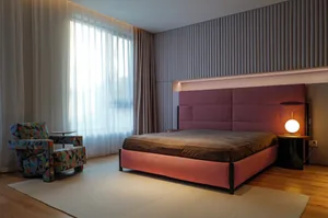 Interior design of a minimalist bedroom featuring a bed with a large burgundy headboard and an armchair with a geometric prin
