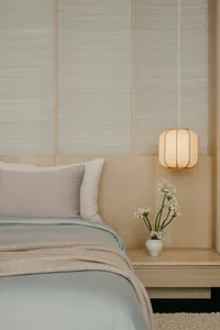 A minimalist bedroom with a bed, pillows, and a hanging lamp with flowers on a nightstand.